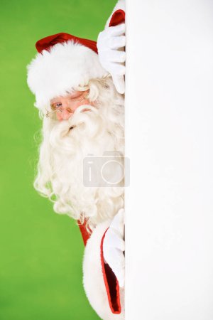 Photo for Santa claus, hiding and wall portrait for Christmas celebration, mockup space or wink. Male person, secret peek and emoji face for festive seasons or holiday, green studio background or signboard. - Royalty Free Image