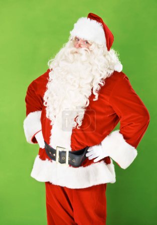 Photo for Santa claus, hands and hips in studio portrait for holiday celebration, festive season or gift giving. Father Christmas, face and costume suit for winter vacation fun, on green background for joy. - Royalty Free Image