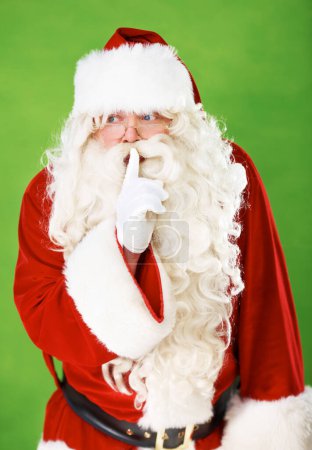 Photo for Santa claus, finger and quiet secret in studio for Christmas surprise, celebration or holiday excitement. Male person, hand gesture and hush emoji for winter vacation joy, green background or mockup. - Royalty Free Image
