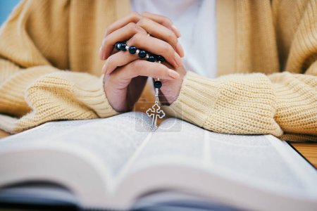 Photo for Bible, rosary and hands of woman in prayer, studying religion at desk in home with Christian faith and knowledge of God. Reading, hope and girl at table with holy book for praise, gospel and beads - Royalty Free Image