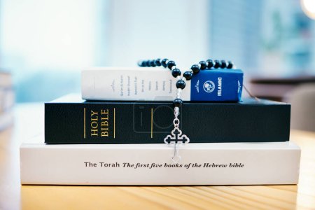 Photo for Books, stack and closeup on table for faith, Abrahamic religion or rosary with crucifix for study in home. Knowledge, holy spirit and education with cross for Jesus, Muhammad or Moses with solidarity. - Royalty Free Image
