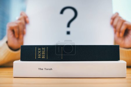 Photo for Books, stack and closeup on desk for faith, Abrahamic religion and question mark on poster for study in home. Person, holy spirit and education for choice with Jesus, Moses and worship God with sign. - Royalty Free Image