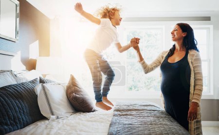 Photo for Family, pregnant woman and her son jumping on the bed while in their home together. Flare, love or smile and a boy child playing in the bedroom with his happy parent for freedom, fun or bonding. - Royalty Free Image