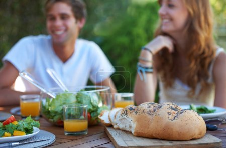 Photo for Friends, bread and food in backyard for lunch and appetizer with a smile and snacks. Salad, talking and young people outdoor of a home with drinks and funny joke together with in summer with meal. - Royalty Free Image