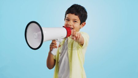 Photo for Communication, face or child with megaphone for news, opinion or sale announcement on blue background. Happy, pointing or young boy talking on loudspeaker for voice, speaking or attention in studio. - Royalty Free Image