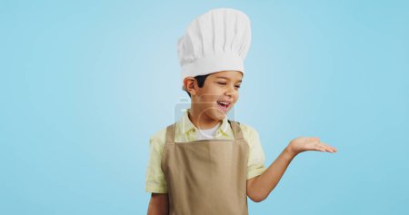Photo for Child, happy face and chef hand to show promotion, advertising or deal in studio. Dress up, profession and young boy happy from future career of cooking and open palm for sale with blue background. - Royalty Free Image