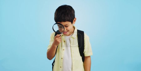 Foto de Busque, mire y un niño con una lupa sobre un fondo azul para inspección o educación. Estudiar, aprender y un niño con herramientas para la investigación, el trabajo detectivesco o curioso con una lente. - Imagen libre de derechos