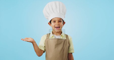 Photo for Child, happy face and chef hand to show promotion, advertising or deal in studio. Dress up, profession and young boy happy from future career of cooking and open palm for sale with blue background. - Royalty Free Image