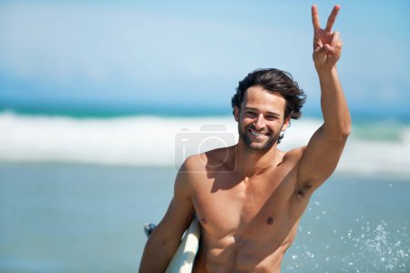 Téléchargez les photos : Surfer, portrait et homme heureux avec les mains paisibles sur une plage pour voyager, la liberté ou l'aventure. Visage, sourire et surfeur masculin avec panneau v en mer pour les sports nautiques, l'entraînement ou les vacances d'été Miami. - en image libre de droit