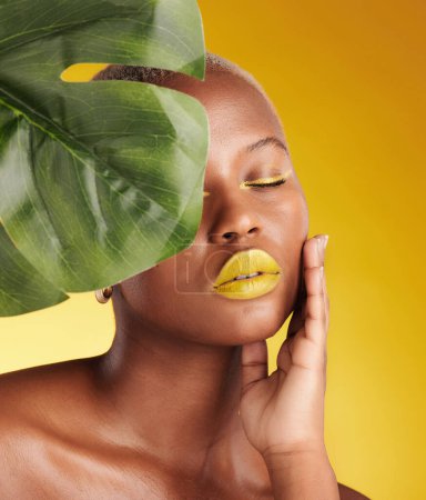 Photo for Beauty, makeup and leaf with face of black woman in studio for tropical, natural and cosmetics. Luxury, sustainability and health with female model on yellow background for plant, salon and wellness. - Royalty Free Image