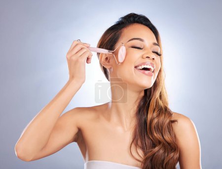 Photo for Happy woman, face roller and massage for skincare, rose quartz cosmetics or salon dermatology on studio background. Female model, crystal stone tools or smile for facial, beauty or lymphatic drainage. - Royalty Free Image