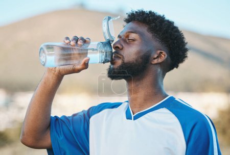 Photo for Black man, fitness or soccer player drinking water in training, exercise or workout in football field. Thirsty, sports or tired athlete on resting break with a healthy beverage for energy to relax. - Royalty Free Image