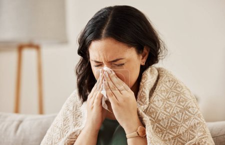 Nose, tissue and sick woman sneezing on a sofa with allergy, cold or flu in her home. Hay fever, allergy and female with viral infection, problem or health crisis in a living room with congestion.