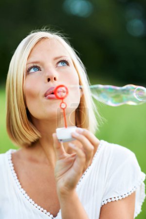 Photo for Woman, thinking and blowing bubbles in nature for fun day or playing at outdoor park. Face of female person or blonde in wonder with stick or wand to blow bubble on playful holiday or summer break. - Royalty Free Image