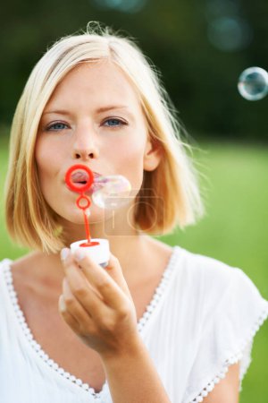 Photo for Woman, portrait and blowing bubbles in nature for fun day or playing at outdoor park. Face of young happy female person or blonde with stick or wand to blow bubble on playful holiday or summer break. - Royalty Free Image