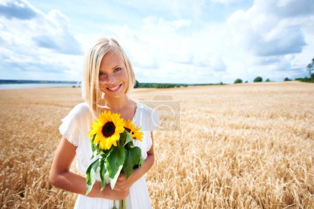 Photo for Happy woman, portrait and flowers in nature countryside on grass or wheat field with cloudy blue sky. Female person or blonde smile with sun flower, plant or blossom in sunshine, travel or vacation. - Royalty Free Image