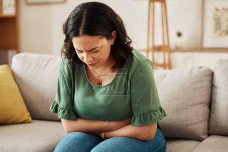 Photo for Stress, stomach pain and woman on a sofa with menstruation, gas or constipation, pms or nausea at home. Gut health, anxiety and lady with tummy ache in living room from ibs, bloated or endometriosis. - Royalty Free Image