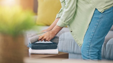 Photo for Hands, home and fold laundry on table for hygiene, cleaning and soft clothes for housework in living room. Woman, fabric and cotton towel on desk for organized house, service and routine in apartment. - Royalty Free Image