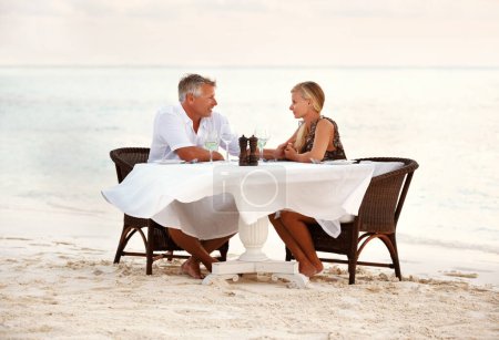 Photo for Beach, dinner and couple with sunset, celebration and romance with anniversary, marriage and tropical island. People, romantic meal or man with woman, ocean and waves with summer holiday and love. - Royalty Free Image