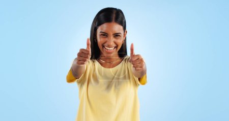 Photo for Woman, happy in portrait and thumbs up for agreement, success or support with hand gesture on blue background. Like, yes and emoji with feedback, vote or opinion in studio with thank you or praise. - Royalty Free Image