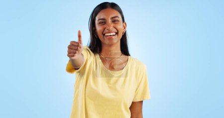 Photo for Woman, smile in portrait and thumbs up for agreement, success or support with hand gesture on blue background. Like, yes and emoji with happiness, vote or opinion in studio with thank you or praise. - Royalty Free Image