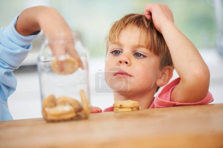 Photo for Cute, cookies jar and boy kid by the kitchen counter eating a sweet snack or treat at home. Smile, dessert and hungry young child enjoying biscuits by a wooden table in a modern family house - Royalty Free Image