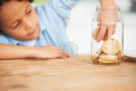 Photo for Hands, cookie jar and boy child by the kitchen counter eating a sweet snack or treat at home. Smile, dessert and cute hungry young kid enjoying biscuits by a wooden table in a modern family house - Royalty Free Image