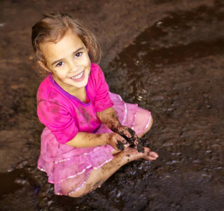 Photo for Girl, child and portrait with happiness in mud for freedom, playing and muddy fun in sunshine weather or outdoor. Kid, female and face of person with smile for activity, enjoyment and relax in dirt. - Royalty Free Image