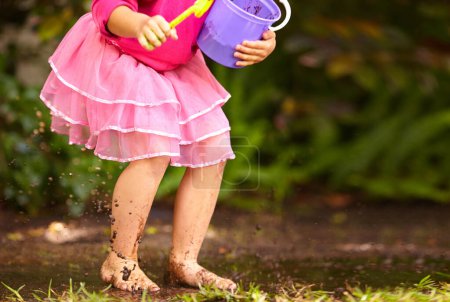 Photo for Legs, girl and kid with toy bucket in muddy puddle for play, explore and child development in garden or backyard. Person, feet or toys in mud water for activity, playing and freedom outdoor in nature. - Royalty Free Image