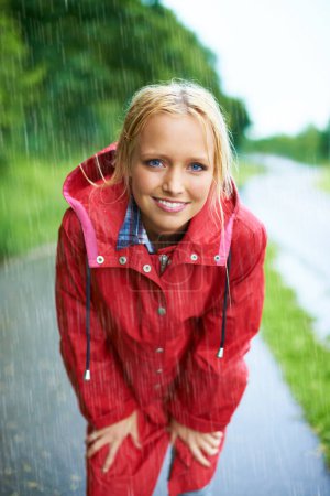 Téléchargez les photos : Sourire, portrait et jeune femme sous la pluie avec manteau dans la nature, la route ou la rue pour l'hiver. Une attitude heureuse et positive et une femme australienne dans la bruine ou la tempête dans la forêt extérieure - en image libre de droit