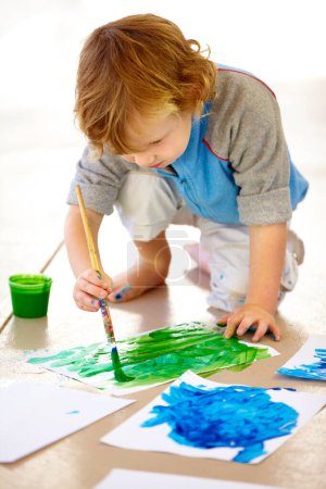 Téléchargez les photos : Art, créatif et un papier à peindre garçon désordonné sur le sol de sa chambre à coucher à la maison pour les devoirs de l'école. Apprentissage, croissance et développement avec un jeune enfant à l'aide d'un pinceau pour la créativité artistique. - en image libre de droit