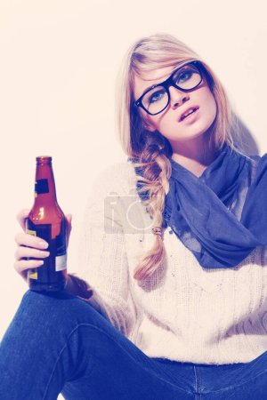 Photo for Portrait, fashion and drinking beer with a woman in studio on a white wall background to relax. Glasses, scarf and glass bottle with a beverage in the hand of a young person for winter celebration. - Royalty Free Image