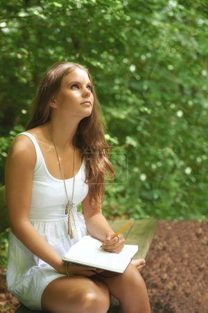 Photo for Park, thinking and a woman writing in a journal outdoor during summer for mental health or expression. Creative, diary and peace with a young person in a green garden to relax for wellness or freedom. - Royalty Free Image