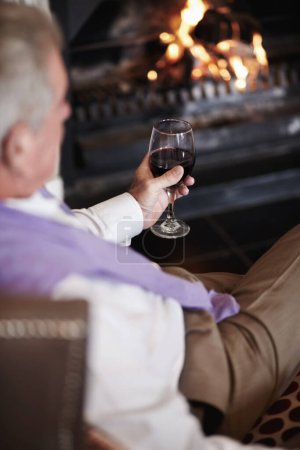 Photo for Relax, senior man with wine at fireplace in hotel lounge or cozy room on retirement vacation. Luxury hospitality, elderly person with glass or drink at holiday accommodation with peace, calm and fire. - Royalty Free Image
