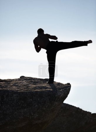 Photo for Karate, kick and fitness man on mountain top for body, power or defense training on blue sky background. Martial arts, MMA and male taekwondo master in nature for exercise, sports or morning cardio. - Royalty Free Image