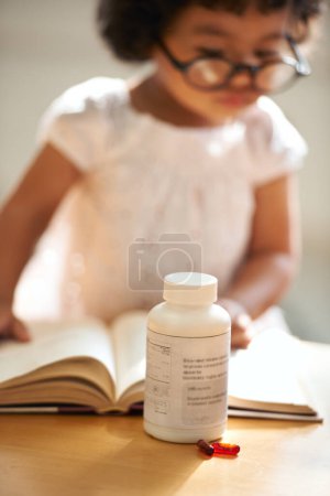 Photo for Girl, child and reading or book concentration or pill bottle adhd diagnosis, learning or development. Kid, glasses and childhood story knowledge discipline, medical pills capsules or school thinking. - Royalty Free Image