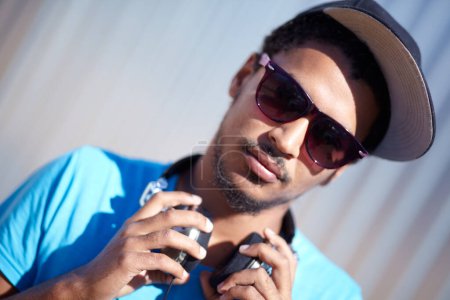 Photo for Portrait, fashion and music with a man in sunglasses outdoor on a blurred background for audio streaming. Face, headphones and hip hop with a confident young person in street wear for urban style. - Royalty Free Image