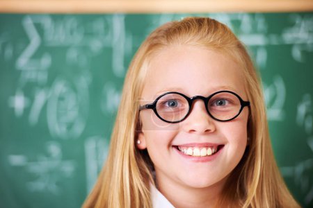 Foto de Retrato de estudiante, niño nerd y feliz por pizarra en clase para aprender conocimientos, educación y estudiar matemáticas. Cara, gafas y sonrisa de friki en la escuela, niña o niño lindo en el aula en Canadá. - Imagen libre de derechos