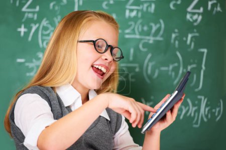 Photo for Girl, calculator and happy for education, learning and problem solving or solution on chalkboard. Smart student, kid or child with glasses and excited for school, typing numbers and math in classroom. - Royalty Free Image