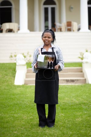 Photo for Black woman, waitress and carrying wine in garden, vinyard or resort in the countryside. Happy African female person with champagne, alcohol or bottle to serve people, reservation or customer service. - Royalty Free Image
