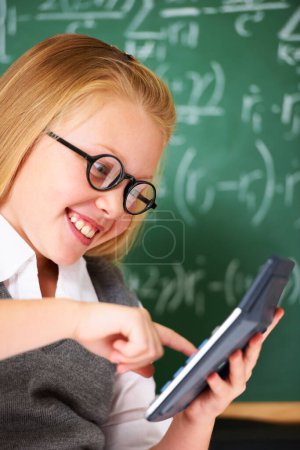 Photo for Child, girl and calculator by chalkboard for happy education, learning and problem solving or solution. Smart student or child with glasses and excited for school, typing numbers or math in classroom. - Royalty Free Image