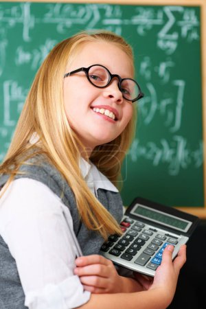 Photo for Smile, calculator and child student in classroom for mathematics homework, lesson or test. Learning, education and portrait of happy young girl kid with glasses and maths equipment by board in school. - Royalty Free Image