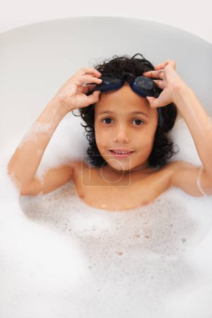 Téléchargez les photos : Portrait, enfants et bain avec un garçon en lunettes tout en nettoyant sa peau à la maison pour une hygiène naturelle. Visage, enfants et un jeune enfant heureux dans la salle de bain pour se laver avec du savon dans l'eau d'en haut. - en image libre de droit