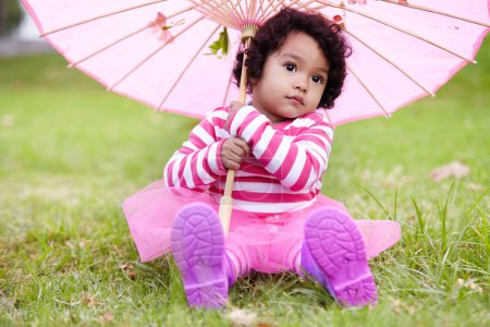Foto de Paraguas, niño lindo y niña en un jardín sentado en la hierba en el fin de semana de verano. Adorable, juguetón y niño pequeño, bebé o niño pequeño con el pelo rizado jugando en el césped en el campo o parque al aire libre - Imagen libre de derechos