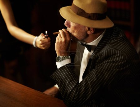 Photo for Businessman, mafia and hold for cigarette in office with woman for light. Gangster, mob or person in suit, bowtie and hat for meeting, criminal activity or job with tobacco for relaxation in space. - Royalty Free Image