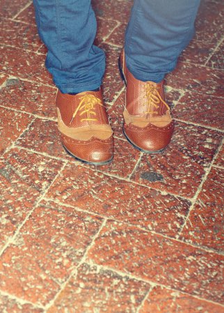 Foto de Zapatos, moda y primer plano de pies de hombre por piso de ladrillo para un atuendo elegante, elegante y de moda. Piernas, calzado y zoom de hombre con estilo lujoso, elegante y caro con jeans por pavimento - Imagen libre de derechos