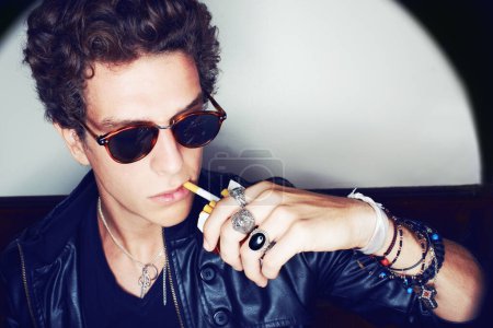 Photo for Portrait of man with cigarette, rock fashion and rockstar attitude on white background in spotlight. Cool punk style, grunge and smoking, confident and handsome male model in studio with sunglasses. - Royalty Free Image