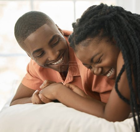 Foto de Afectuosa pareja afroamericana joven tomados de la mano mientras se relajan juntos en una cama en casa. Feliz novio negro y novia compartiendo momentos íntimos en una relación amorosa mientras se une. - Imagen libre de derechos