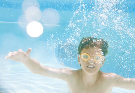 Foto de Pero no solo es divertido, nadar también proporciona un montón de beneficios para la salud. un niño pequeño con gafas de natación mientras nada bajo el agua - Imagen libre de derechos
