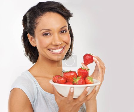 Téléchargez les photos : Santé, fraises et portrait de femme dans un studio de bien-être, nutrition et alimentation biologique. Sourire, vitamines et femme du Mexique manger des fruits pour une collation végétalienne saine par fond gris - en image libre de droit